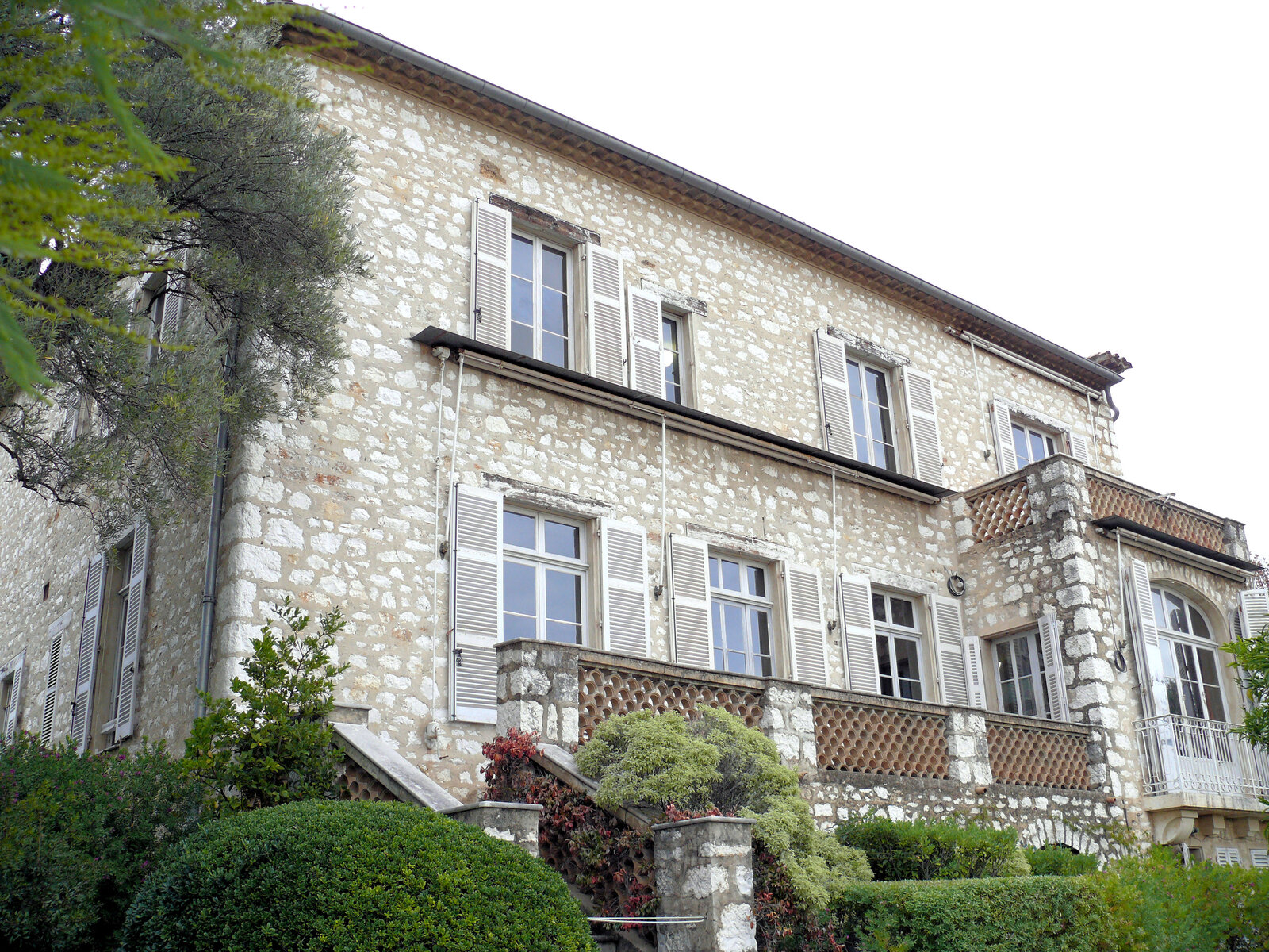 Façade en pierre de la villa de Renoir aux Collettes, volets et balcon, entourée de buissons