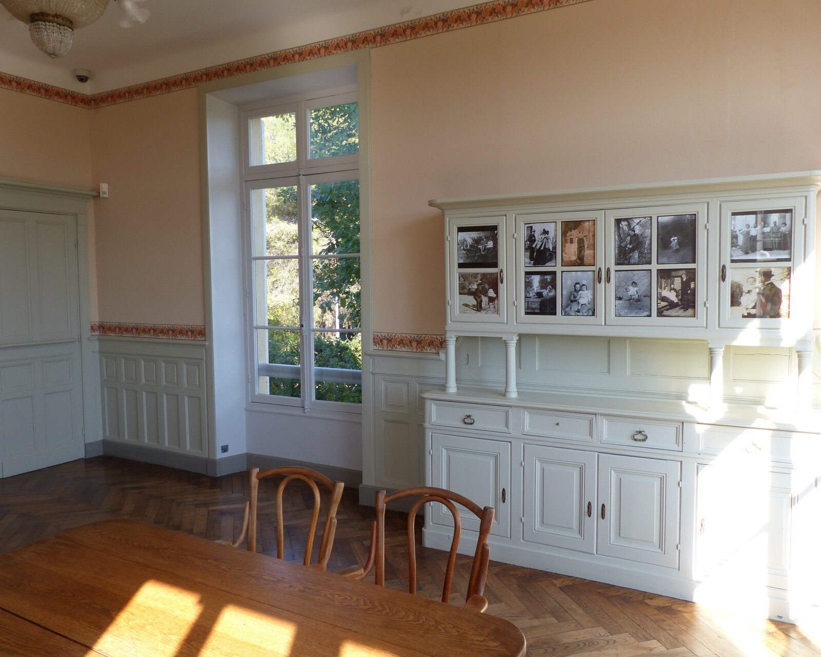 Pièce lumineuse de la maison de Renoir aux Collettes, parquet, table et chaises, vitrine de photographies anciennes