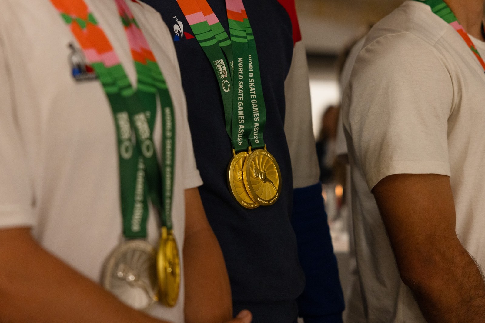Gros plan sur des médailles d’or World Skate Games ASU26 accrochées au cou d’athlètes français en polo Le Coq Sportif