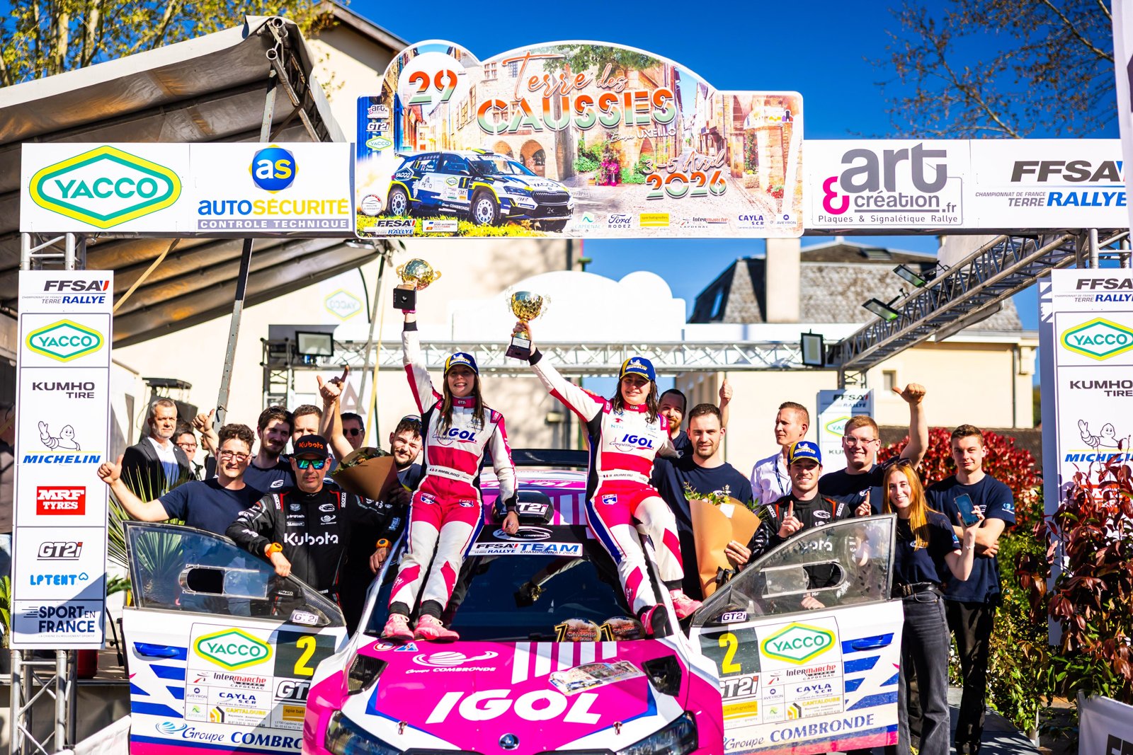 Sarah Rumeau et Julie Amblard debout sur le capot de leur Škoda rose, trophées levés, entourées de leur équipe au Terre des Causses