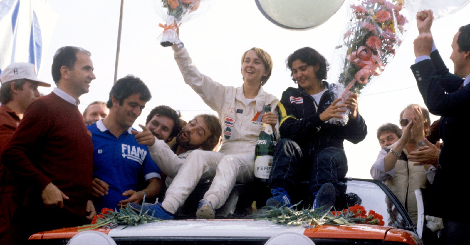 Michèle Mouton et Fabrizia Pons fêtent leur victoire, bouquets de fleurs à la main, debout sur leur Audi quattro entourées de la foule