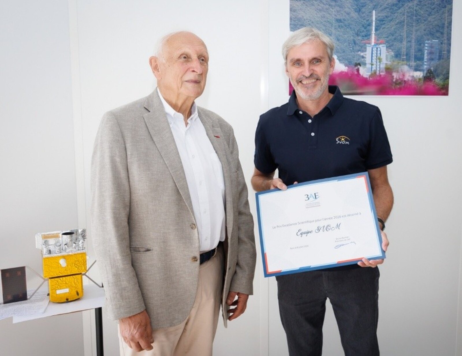 Hervé Austruy, en veste beige, aux côtés de Bertrand Cordier, souriant, qui tient le diplôme « Équipe SVOM »