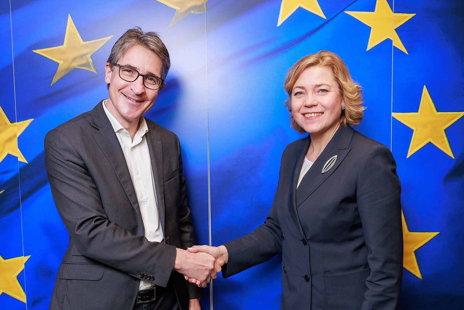 Patrice Caine serrant la main d’une responsable devant un drapeau européen