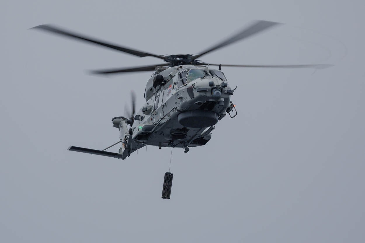 Un hélicoptère NH90 en vol stationnaire, un sonar trempé suspendu sous la cabine