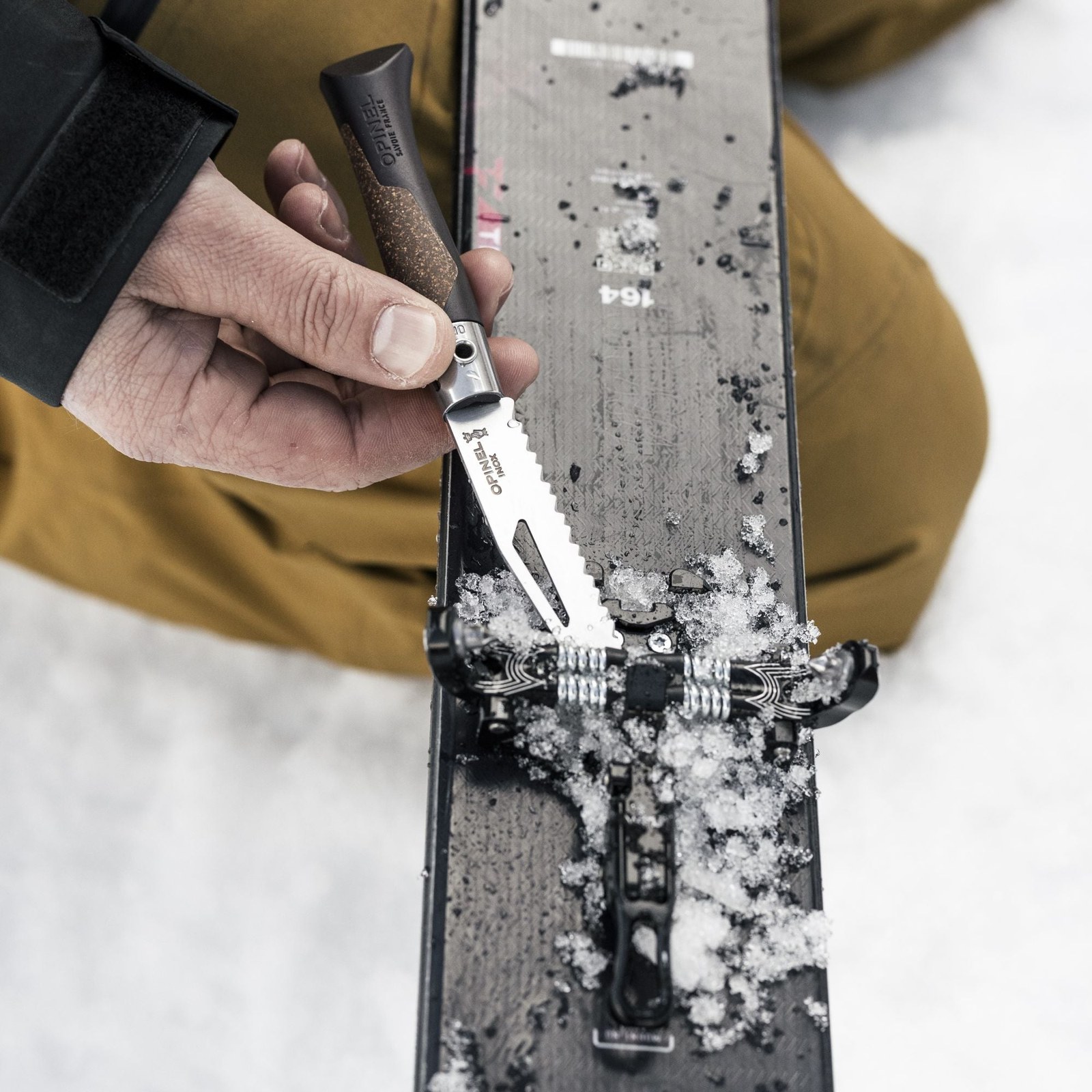 Une main règle une fixation de ski enneigée avec le couteau Opinel Néo7 Alpine