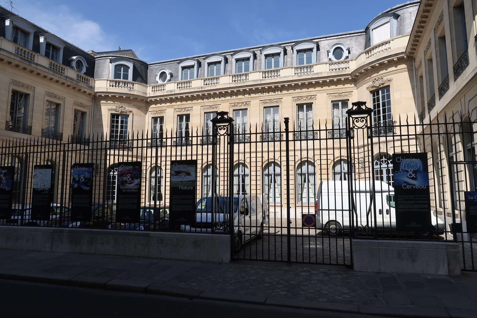 La façade et la grille de la Maison de la Chimie, rue Saint-Dominique à Paris, sous un ciel bleu