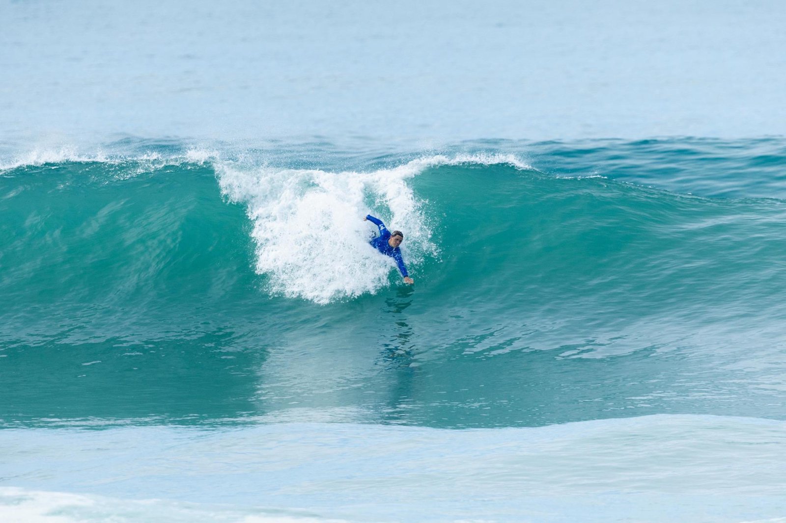 Niels Schorsch glisse sous la lèvre d’une vague qui déferle, le bras tendu
