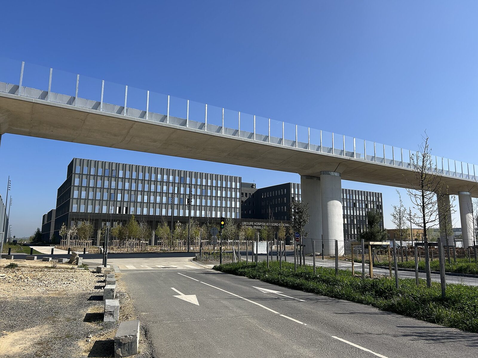 Le viaduc passe au-dessus d’une route neuve devant un grand bâtiment hospitalier vitré