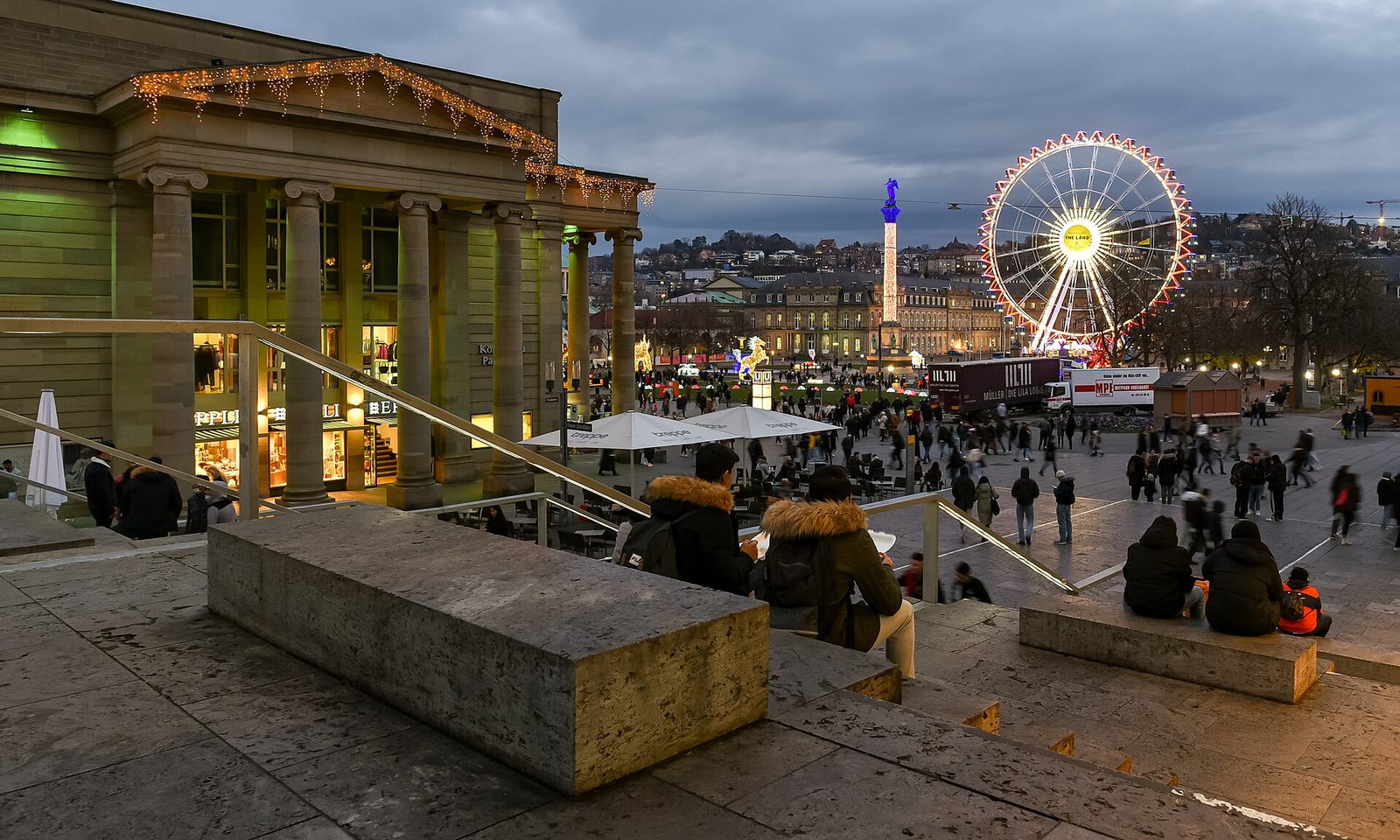 La Schlossplatz de Stuttgart à la tombée de la nuit, avec le Nouveau Château, une colonne et une grande roue illuminée