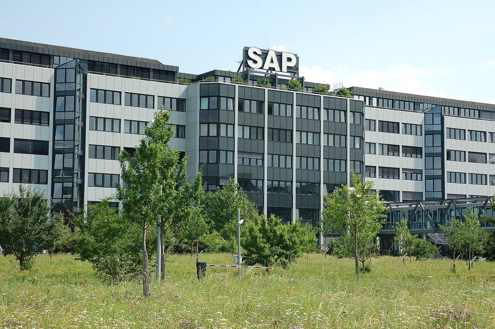 Immeuble de bureaux vitré du siège de SAP à Walldorf, avec le logo SAP sur le toit, devant une pelouse arborée