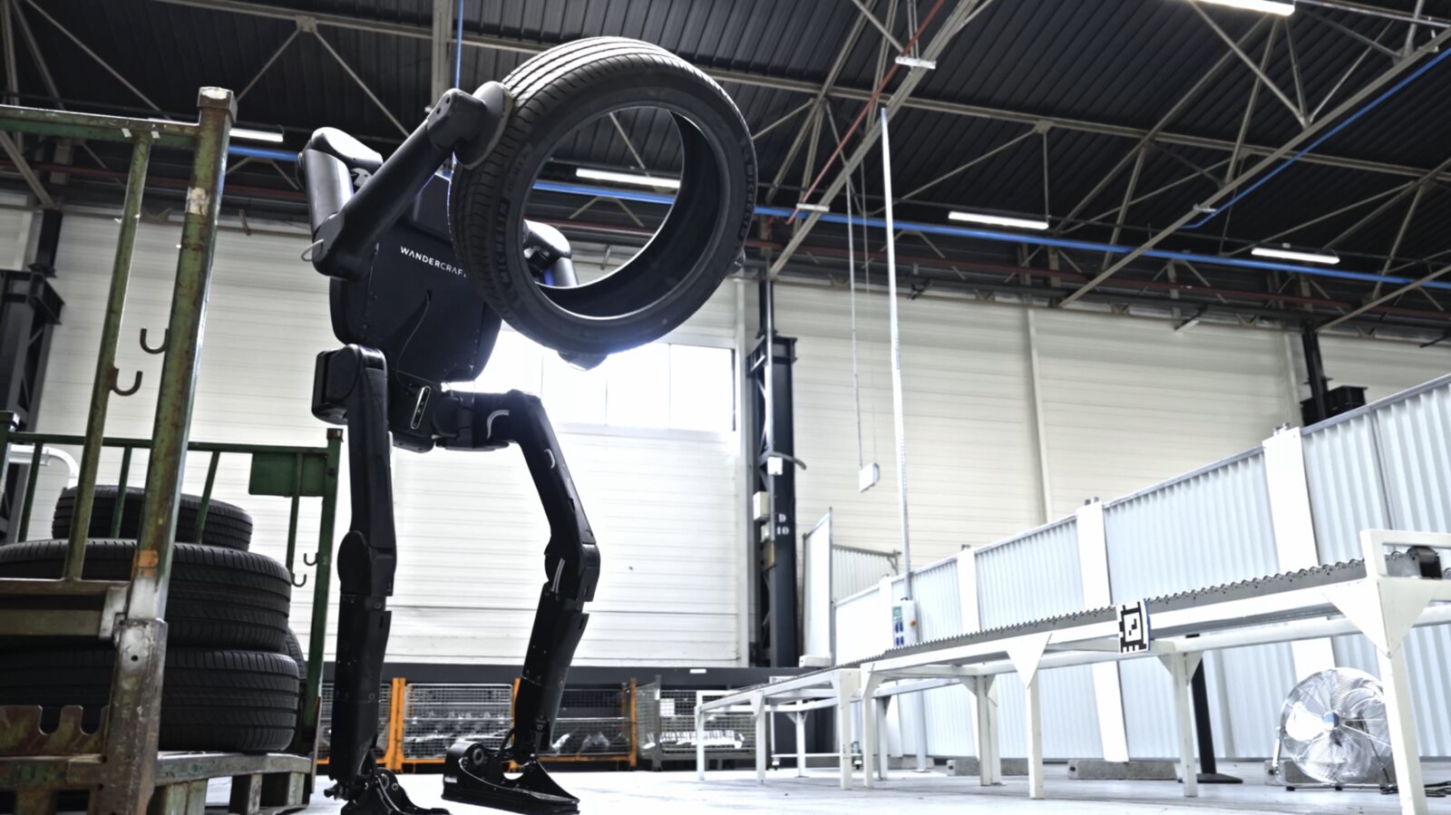 Calvin-40 transporte un pneu à bout de bras dans un entrepôt industriel
