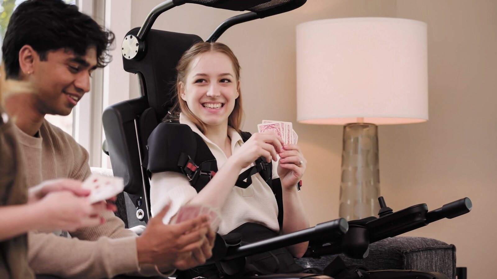 Une jeune femme sourit en jouant aux cartes, installée dans un exosquelette Wandercraft, face à un ami