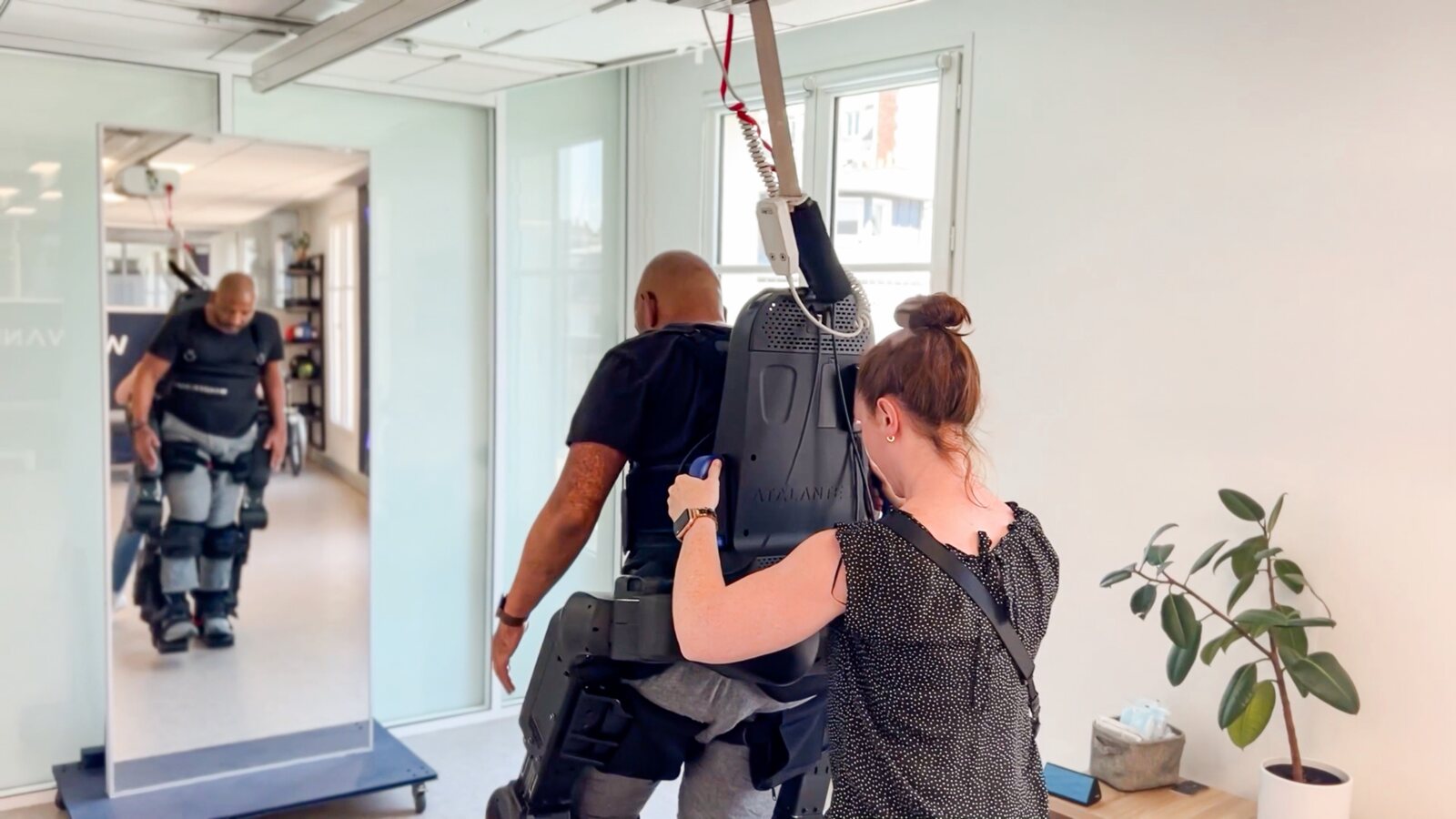 Une kinésithérapeute accompagne un patient équipé de l’exosquelette Atalante dans un centre de rééducation