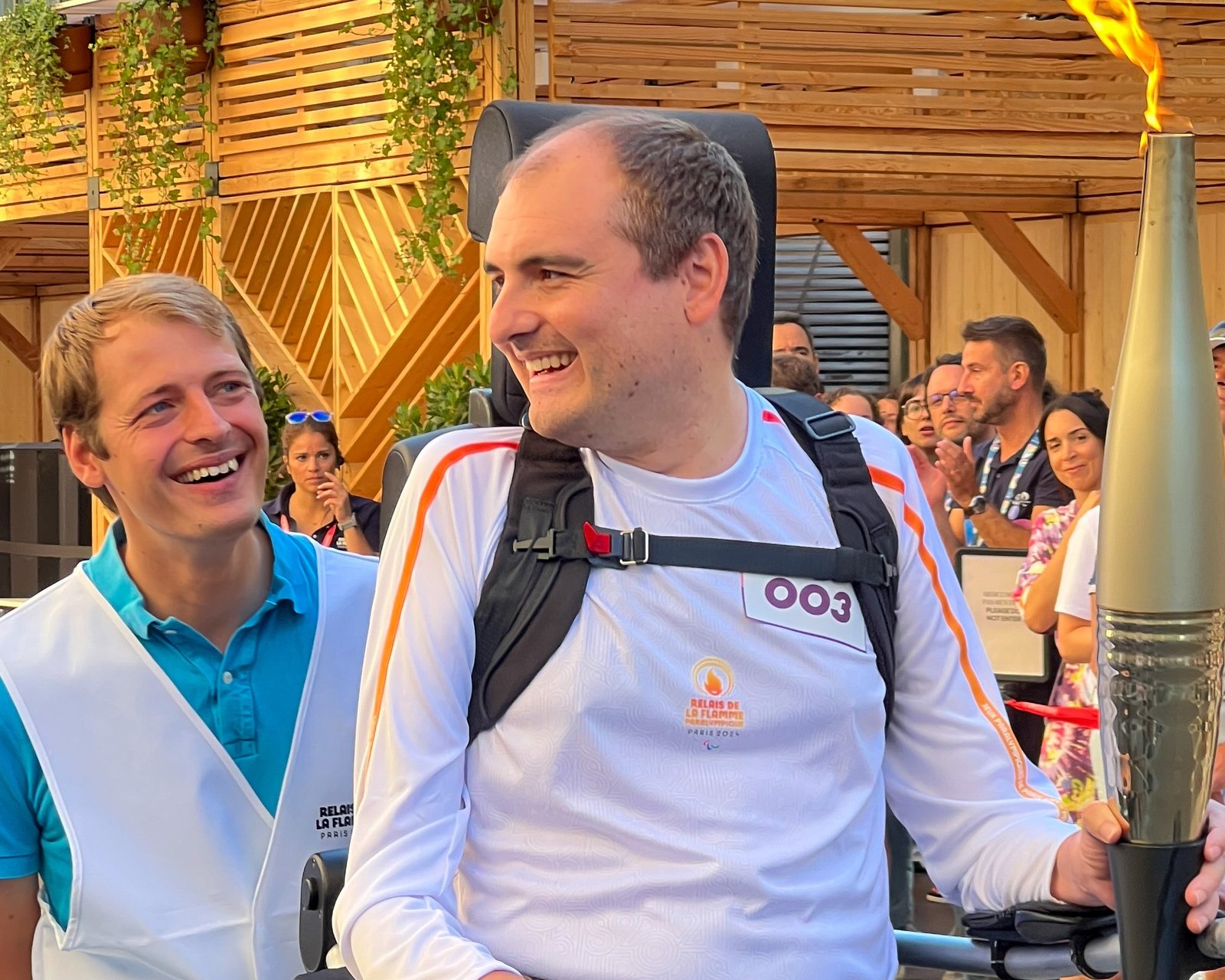 Thibault Simon, en tenue blanche du relais de la flamme, rit aux côtés de son frère Nicolas Simon, la torche paralympique à la main