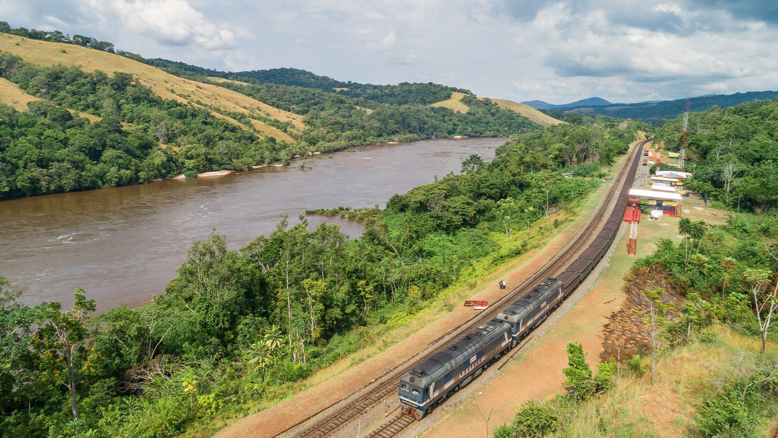 Un long train de minerai de la Setrag longe un fleuve au cœur de la forêt gabonaise