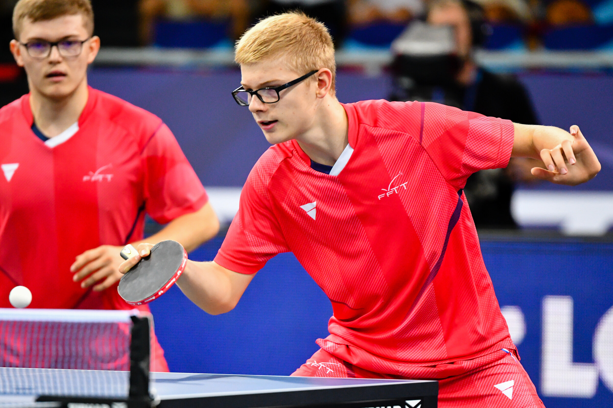 Félix et Alexis Lebrun, maillots rouges FFTT, en action côte à côte derrière la table bleue