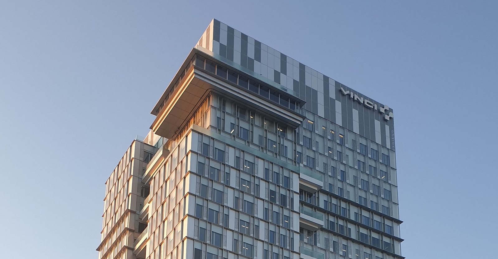 Le haut de la tour de verre du siège de VINCI à Nanterre, avec le logo VINCI, sous un ciel bleu